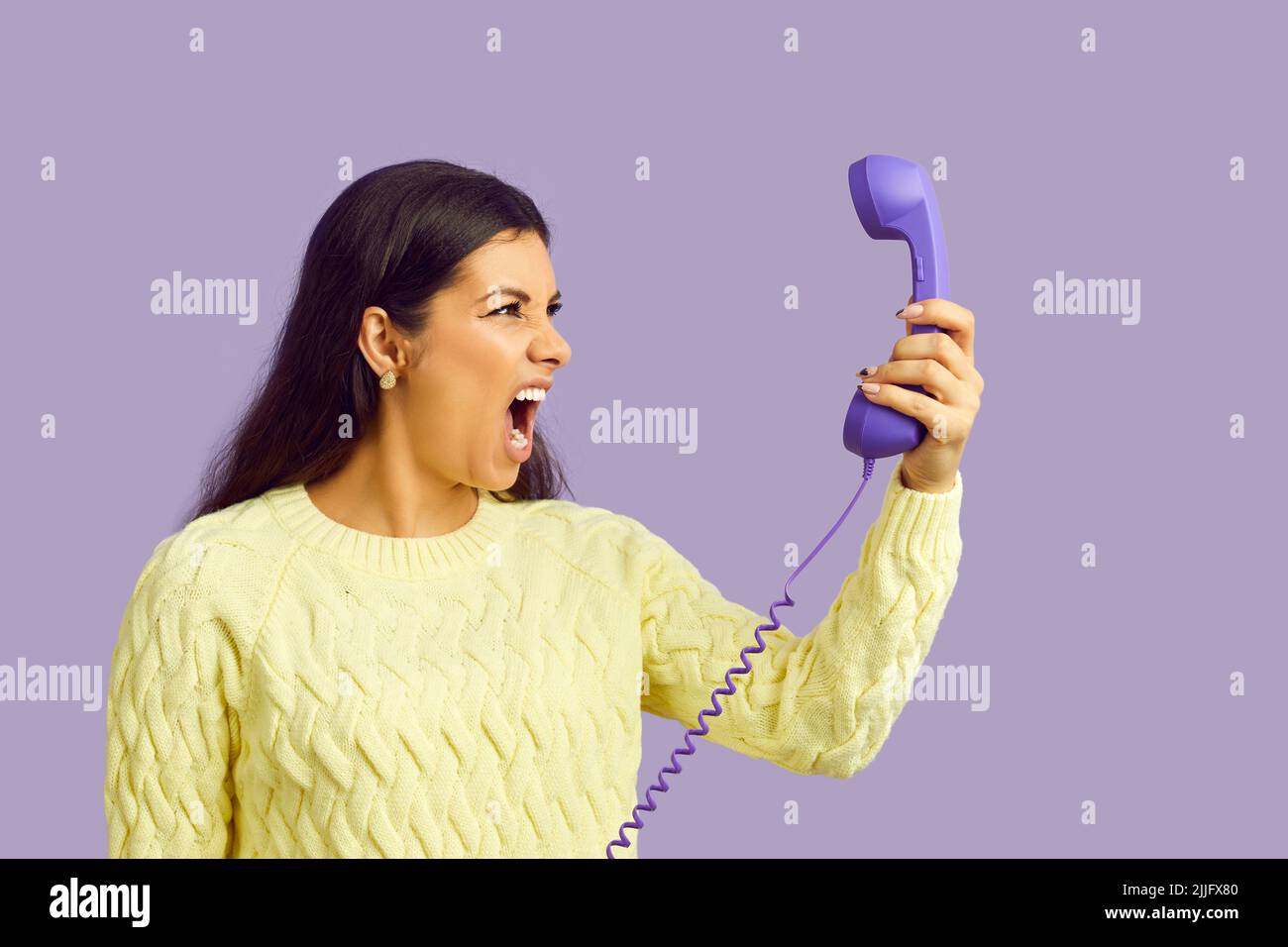 Junge Frau hält Festnetztelefon und schreit nervös über Anrufe mit lästiger Werbung Stockfoto