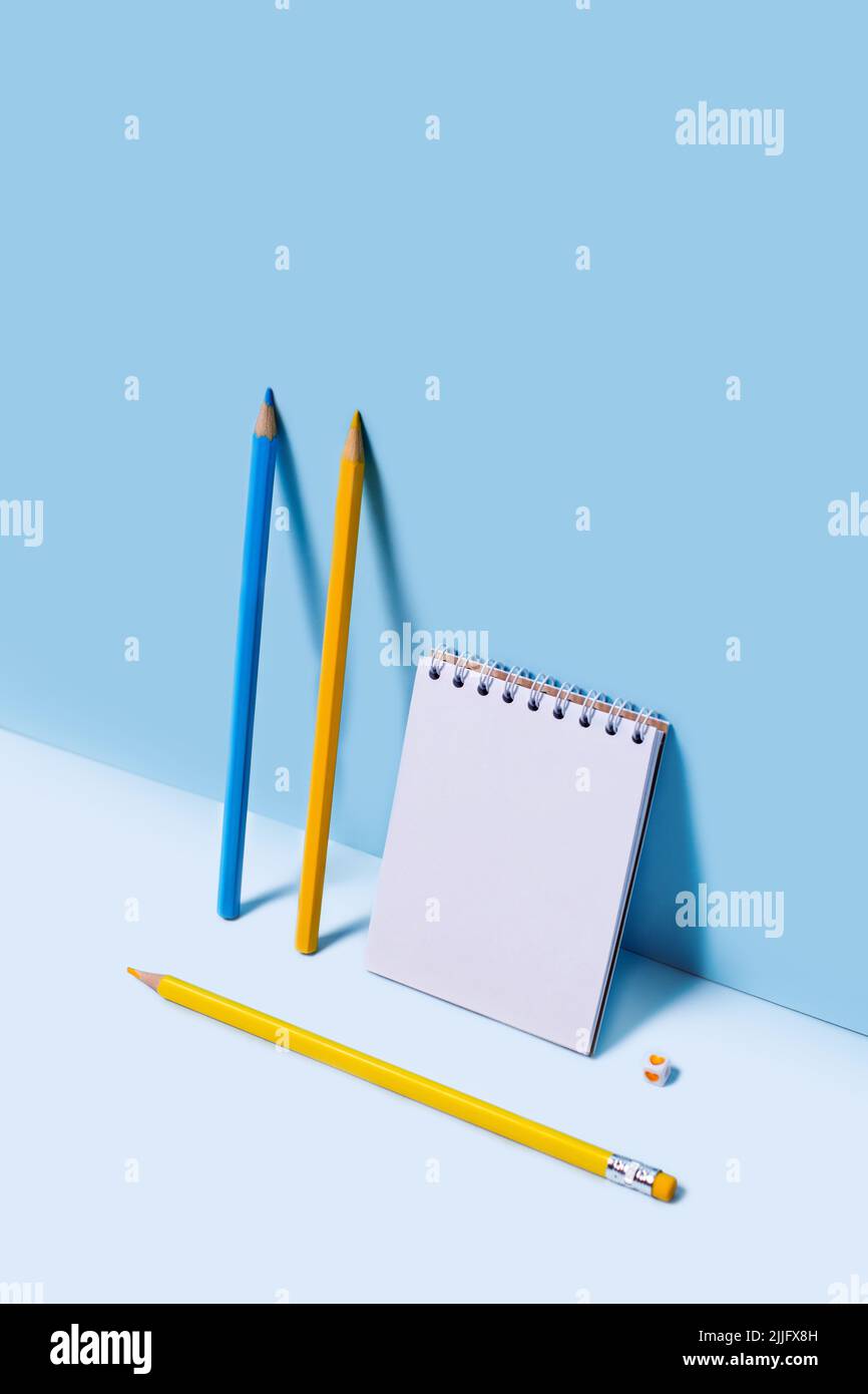 Vertikales Frontalfoto mit Notizbuch und Bleistiften, die an der blauen Wand gelehnt sind. Stockfoto