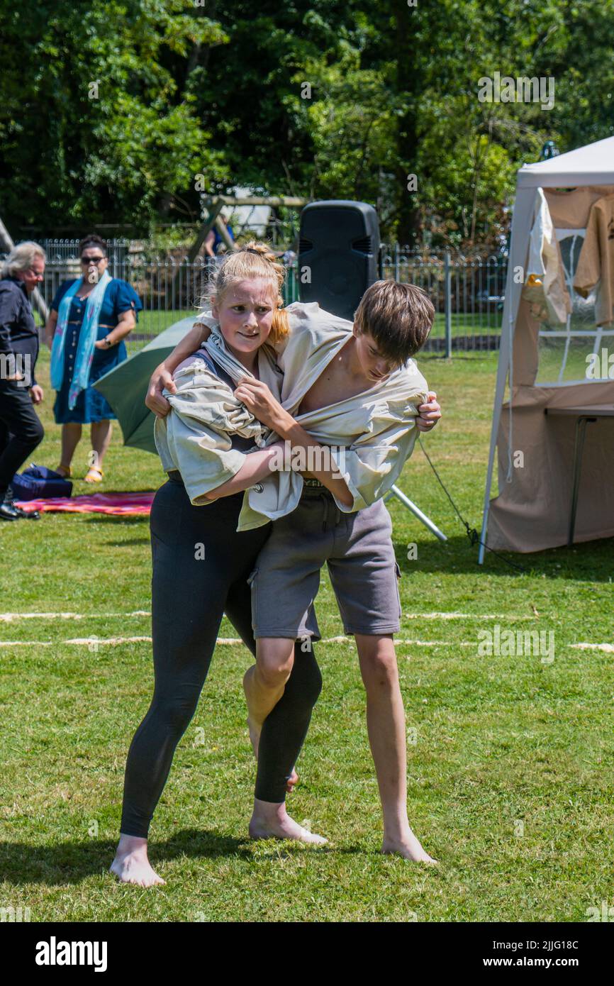 Ein junges Teenager-Mädchen, das mit einem Jungen kämpft, der beim Grand Cornish Wrestling Tournament auf dem malerischen Dorfgrün von St. Mawgan in Pydar i teilhat Stockfoto