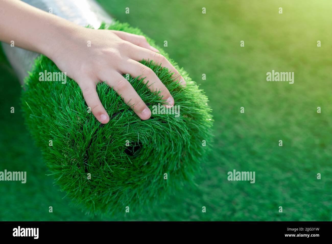Selektiver Fokus einer Hand streichelt eine Rolle von weichem, spritzig Kunstrasen. Kostengünstige Alternative für grünen Rasen Stockfoto