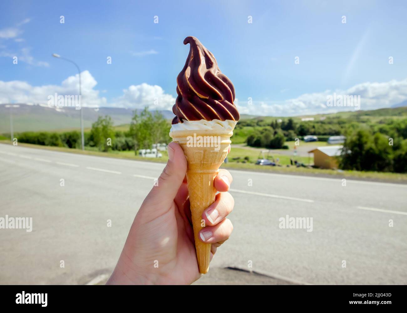 Hand hält leckere isländische lokale Soft-Serve-Vanille-Eis in heißer Schokolade getaucht, Island Natur auf dem Hintergrund. Stockfoto