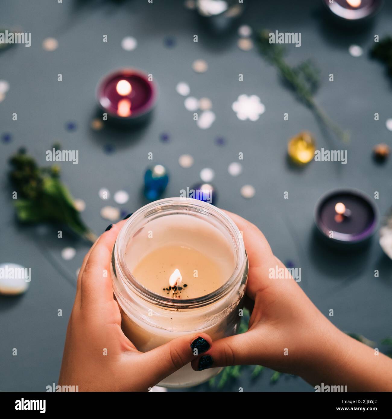 Die Hände im New Year Party-Dekor halten eine Kerze im Licht Stockfoto