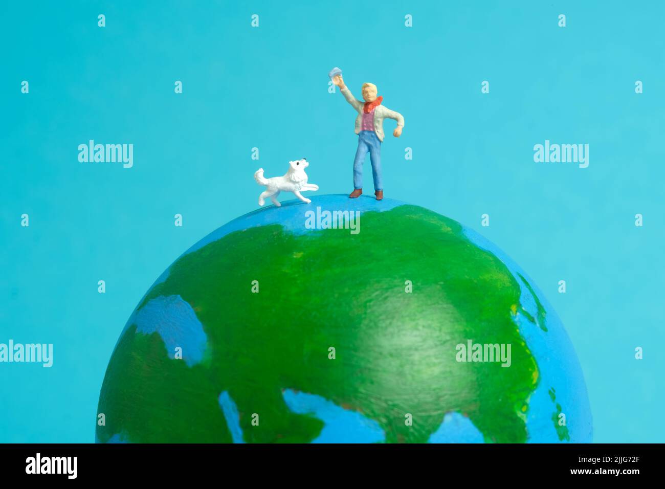 Miniatur Menschen Spielzeug Figur Fotografie. Konzept für den internationalen Kindertag. Ein Kind spielt mit Hund über der Erde Globus, isoliert auf blauem Hintergrund. Bild Stockfoto
