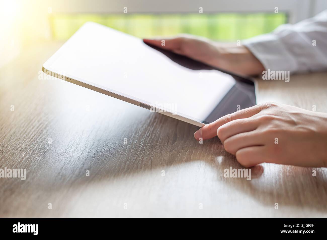 Tablet mit einem leeren Bildschirm in den Händen auf einem Holztisch Stockfoto