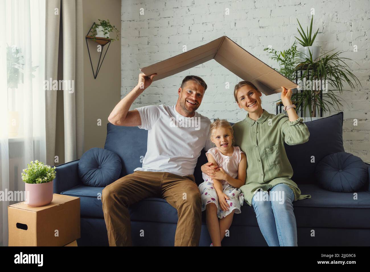 Glückliche Familie mit Kind hält Pappdach über Kopf. Neues Haus und Hypothek-Konzept Stockfoto