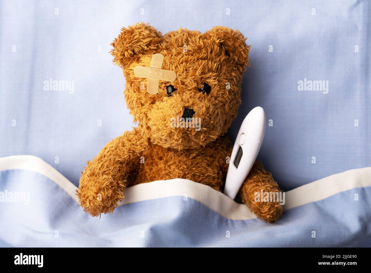 Kranker Teddybär auf Krankenhausbett mit Thermometer und Pflaster auf dem Kopf. Konzept der Kinder- und Kindermedizin Stockfoto