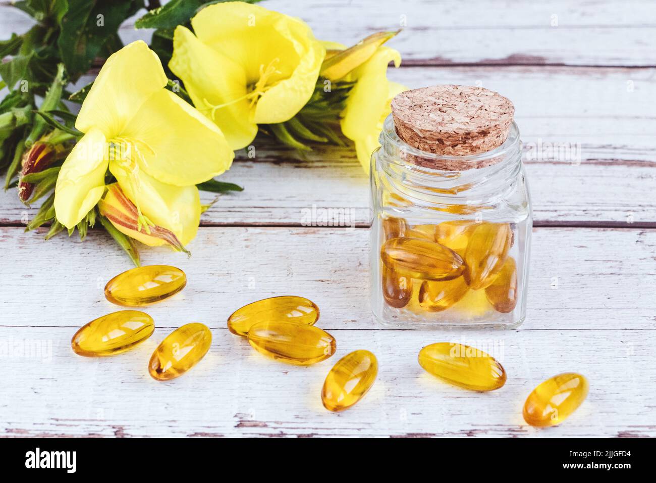 Nachtkerzenöl-Gel-Kapseln in Glasflasche, Pillen und gelbe Blumen auf Holztisch Stockfoto