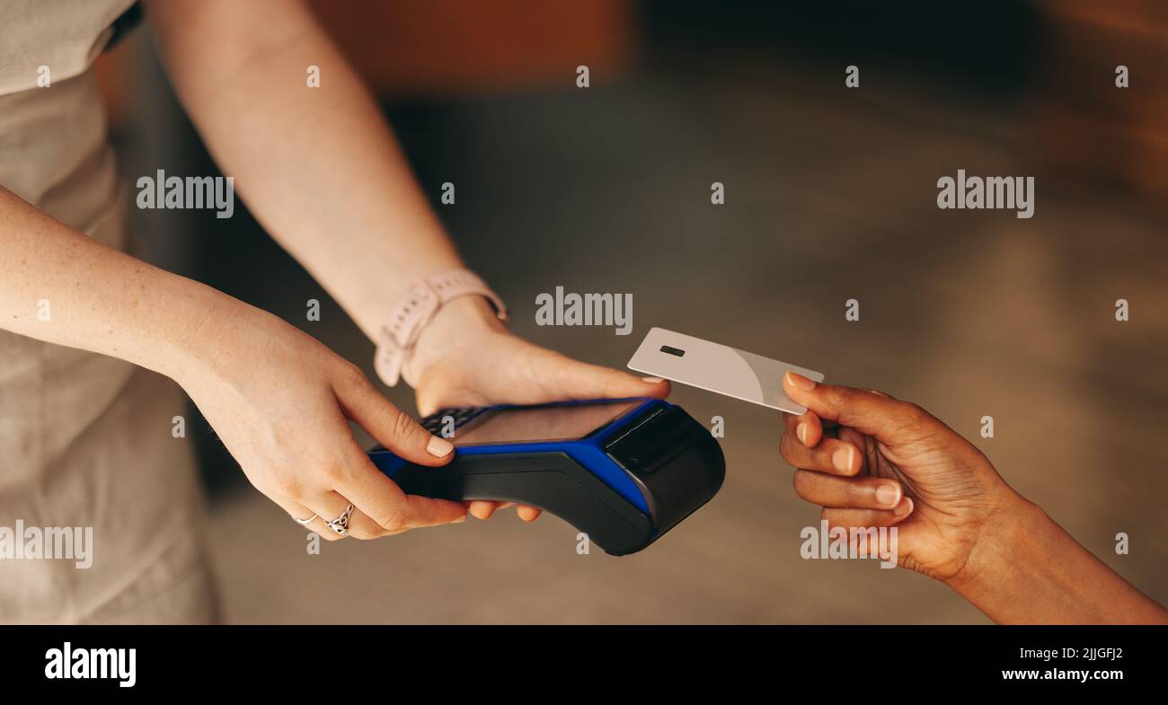 Nicht erkennbarer Kunde scannt seine Kreditkarte auf einem Kartenautomaten, um ihre Rechnung in einem Café zu bezahlen. Frau, die eine bargeldlose und kontaktlose Transaktion mit macht Stockfoto