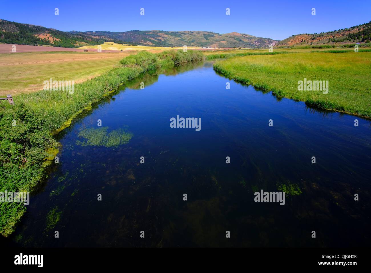 Blauer Streifen oder Fluss aus fließendem Wasser im Tal, der blauen Himmel und Wolken reflektiert Stockfoto