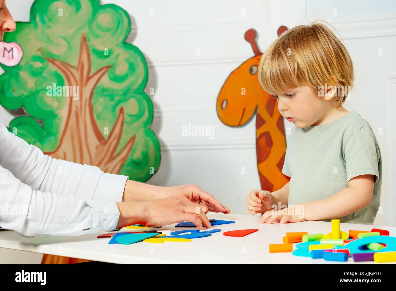 Junge mit Erwachsenen im Kindergarten legte Figuren auf den Tisch Stockfoto