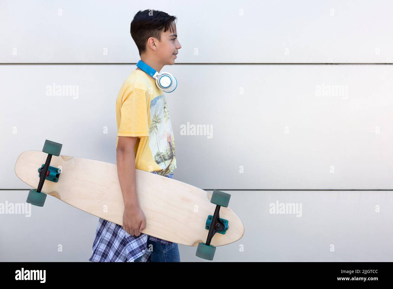 Lächelnder kaukasischer Teenager mit Skateboard in der Hand. Er ist an einer Wand isoliert. Urbane Lebensart. Platz für Text. Stockfoto