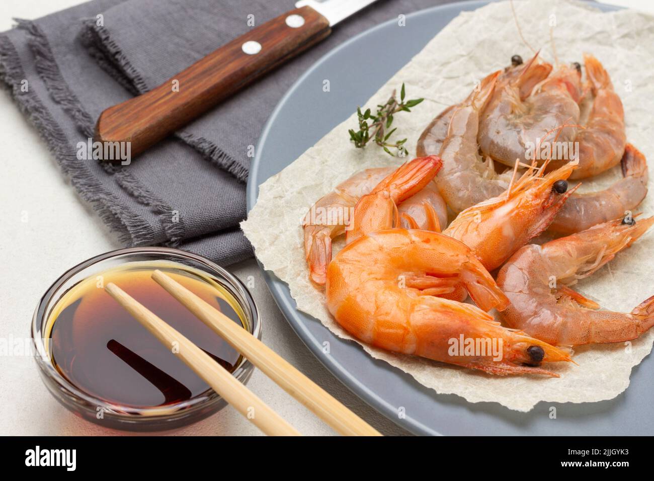 Garnelen auf Papier auf grauem Teller. Sojasauce in Glasschüssel und Essstäbchen. Messer auf grauer Serviette. Nahaufnahme. Weißer Hintergrund Stockfoto