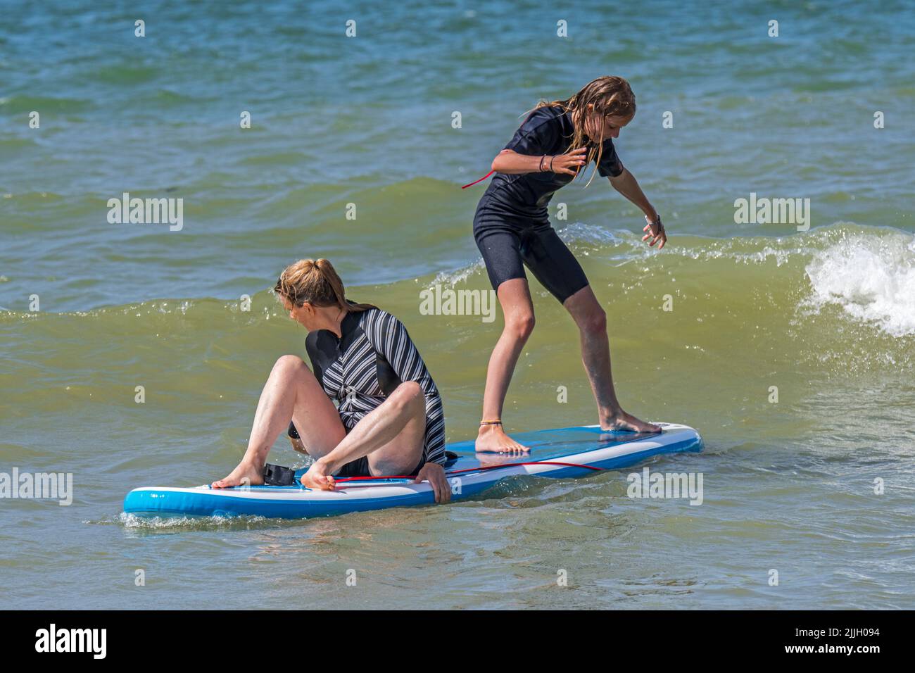 Stand-up-Paddleboarding, zwei ungeschickte Mädchen, die auf dem Paddleboard/SUP-Board auf See trainieren, um ihr Gleichgewicht zu halten Stockfoto