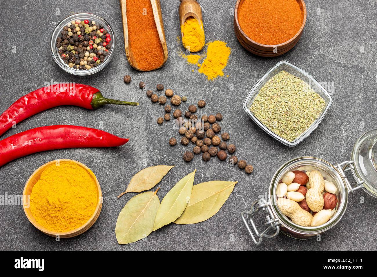 Nüsse im Glasgefäß. Kurkuma und Paprika in Schüsseln und Schaufel gemahlen. Piment und Lorbeerblatt. Frischer roter Pfeffer. Flach liegend. Schwarzer Hintergrund Stockfoto