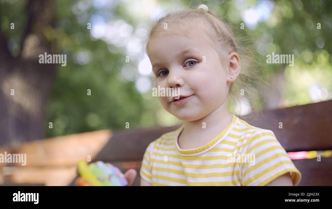 Kleines Mädchen hält einen bunten Lebkuchen und lächelt. Nahaufnahme Porträt von niedlichen Mädchen auf der Parkbank mit Cookies in sieht in die Ca sitzen Stockfoto
