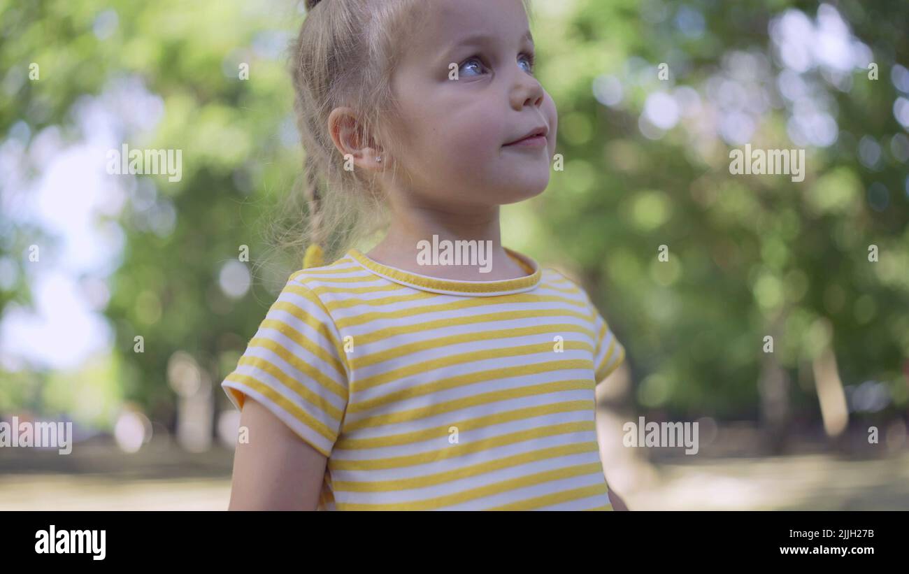 Nettes kleines Mädchen hört Musik und singt mit. Das Nahaufnahme-Porträt eines kleinen Mädchens steht in einem Stadtpark und hört Musik Stockfoto