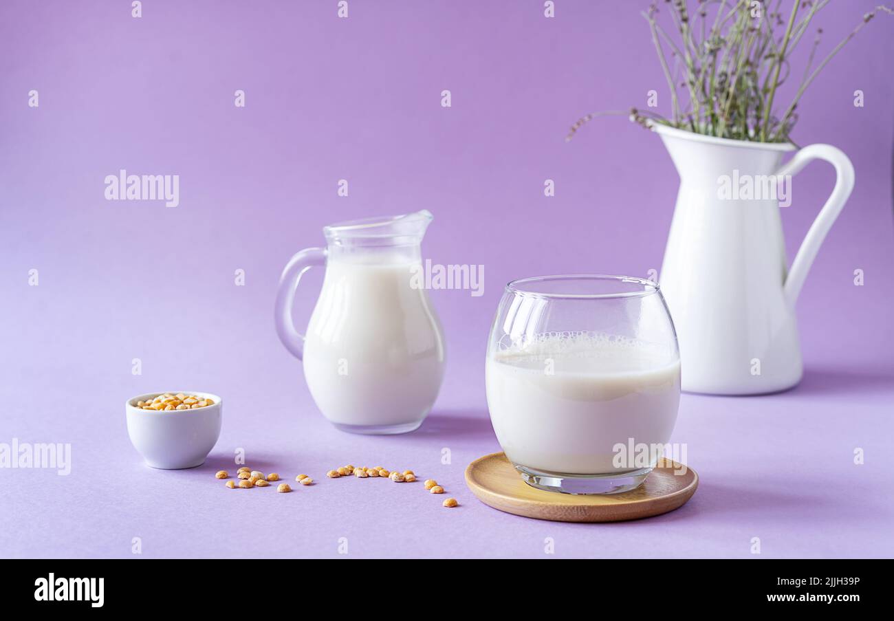 Vegane, gesunde Erbsenmilch in Glas und Glas, Erbsensamen und weißer Krug mit Lavendel. Lila Hintergrund. Speicherplatz kopieren Stockfoto