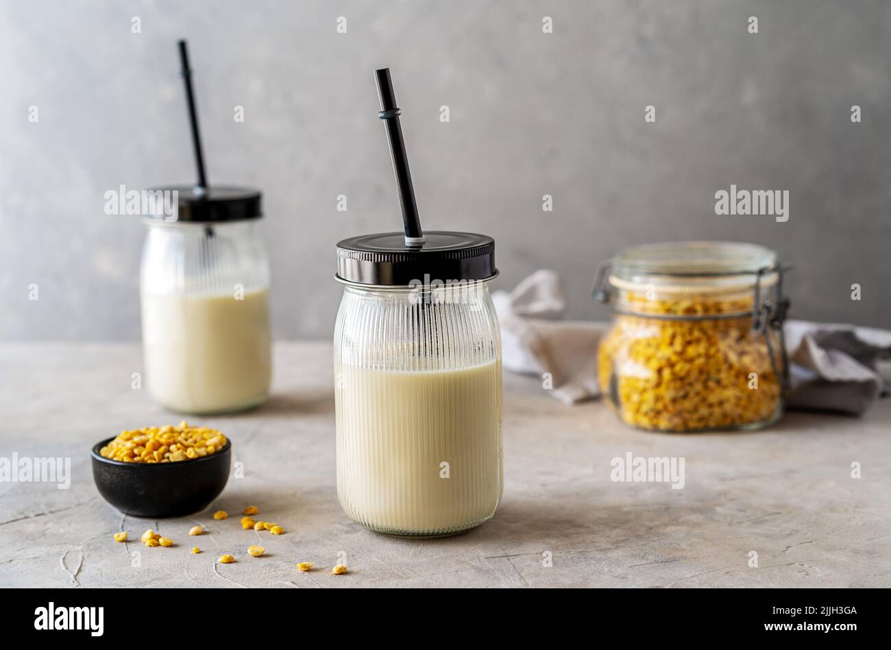 Vegane, gesunde Erbsenmilch in Gläsern mit Trinkhalmen, betontem Hintergrund, Erbsenkörnern und Mockup-Platz Stockfoto