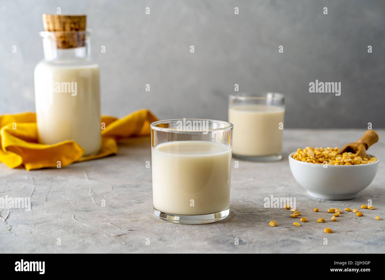 Vegane, gesunde Erbsen-Milch in Glasflasche und zwei Gläsern, betonierter Hintergrund, Erbsen-Körner, gelbe Serviette. Speicherplatz kopieren Stockfoto