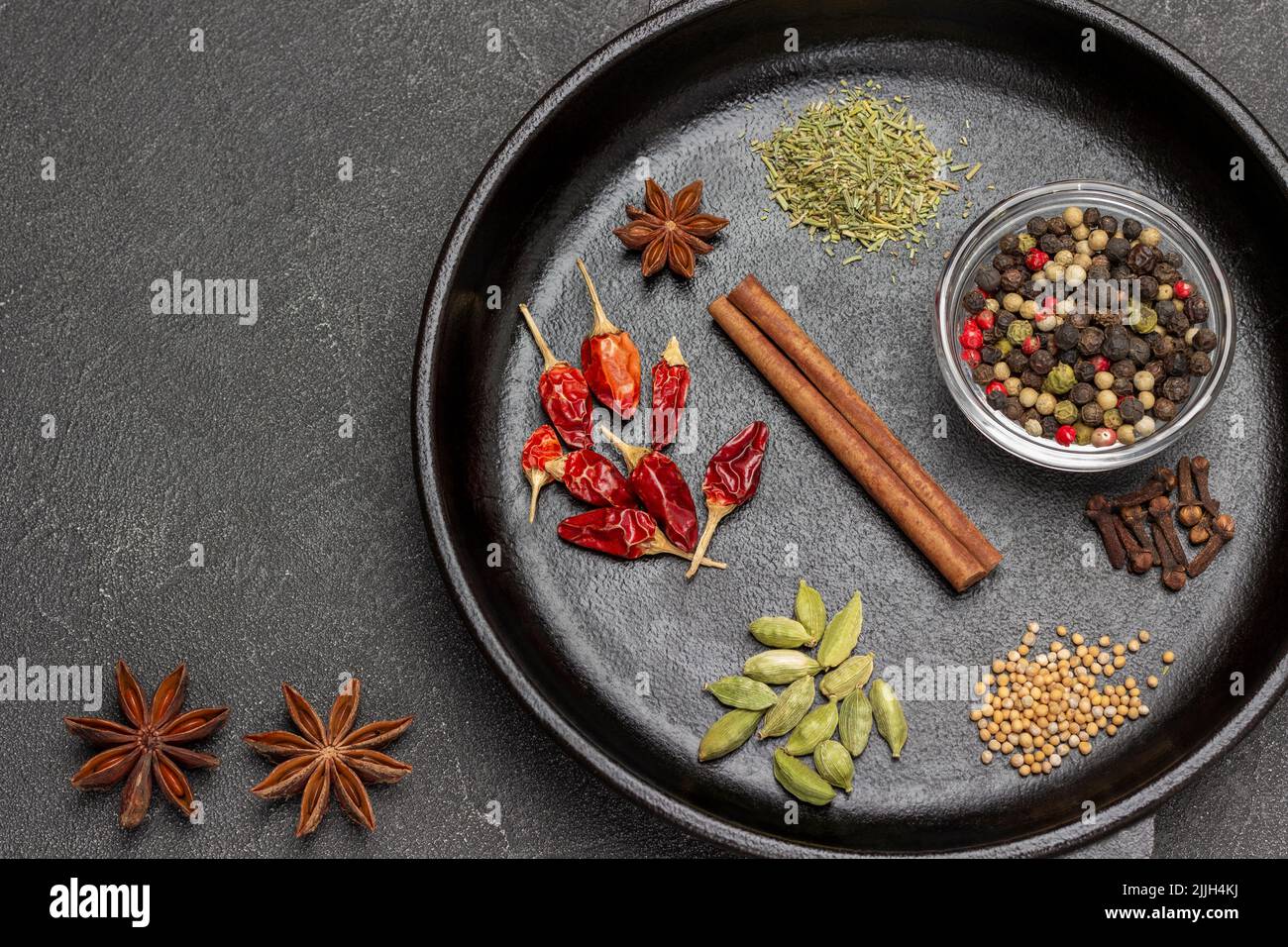 Zimtstange, Koriandersamen, Pfefferschoten, Kardamom und Piment in der Pfanne. Sternanisgestein auf dem Tisch. Draufsicht. Schwarzer Hintergrund Stockfoto