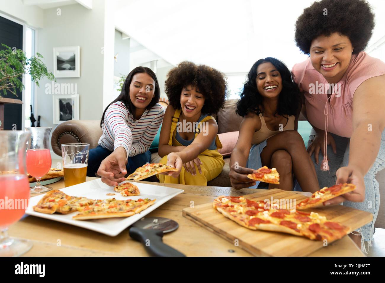 Aufgeregt Biracial weibliche Freunde Kommissionierung Pizza Scheiben auf dem Tisch, während Freizeit zu Hause Stockfoto
