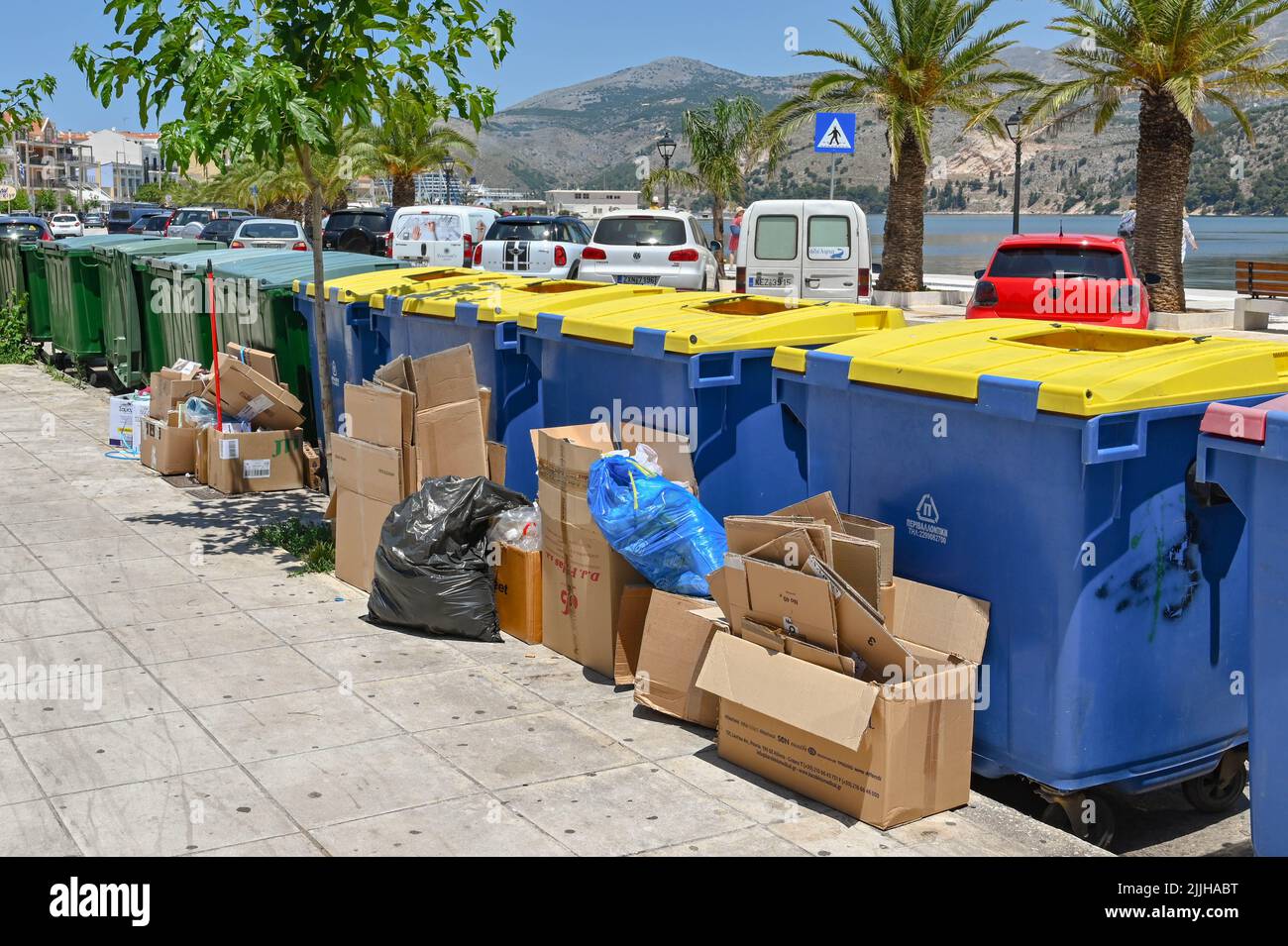 Argostili, Kefalonia, Griechenland - Juni 2022: Ich habe Kartons auf einer Straße in der Stadt gegen große Industrieabfallbehälter gestapelt Stockfoto