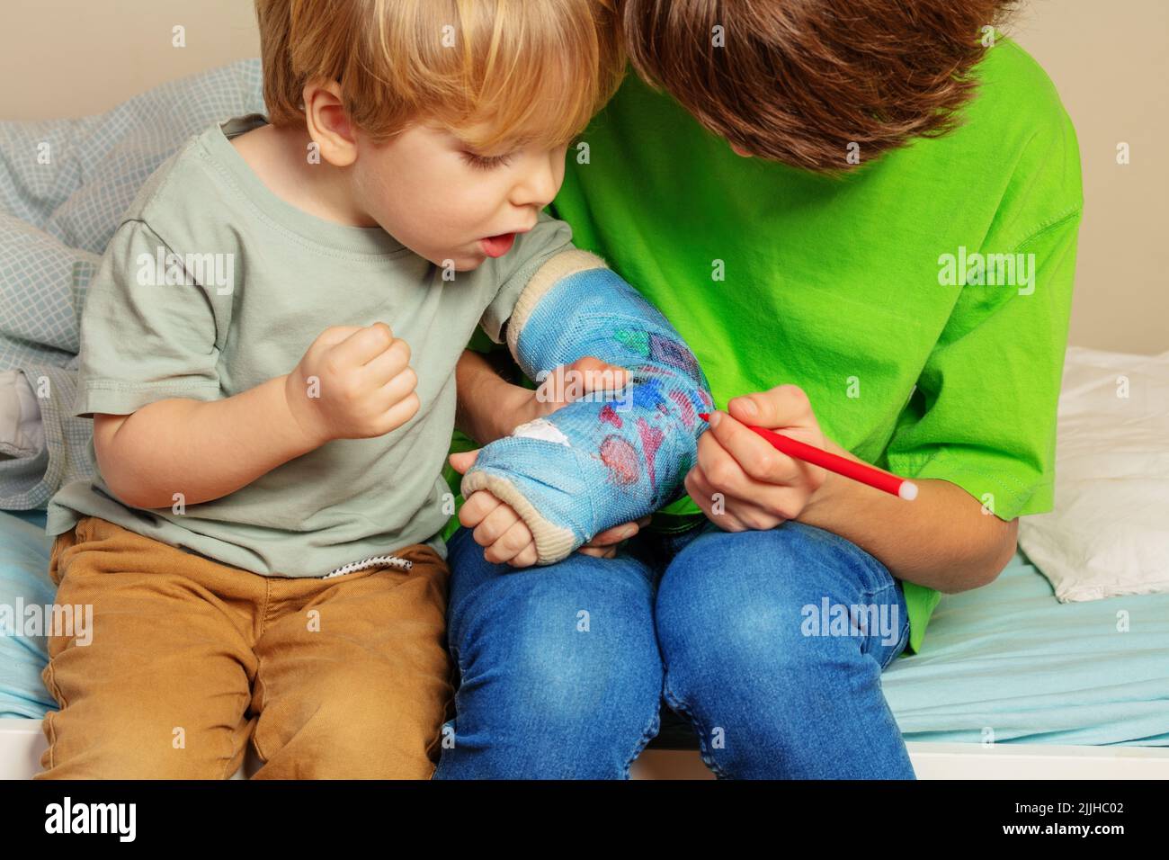 Interessierter Junge schaut Bruder Draw auf seinen gebrochenen Handguß an Stockfoto Interessierter Junge schaut Bruder Draw auf seinen gebrochenen Handguß an Stockfoto