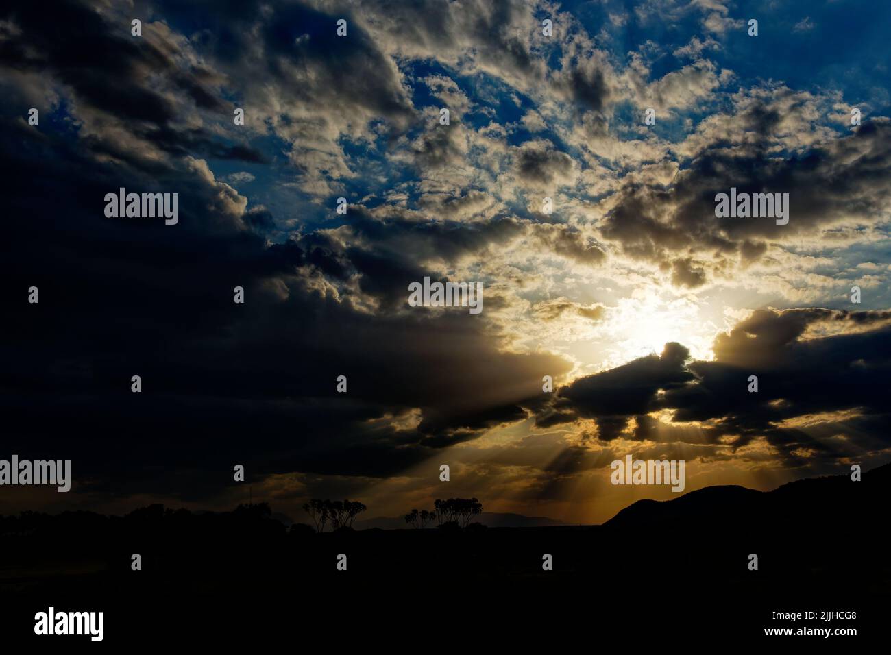 Die untergehende Sonne scheint durch vereinzelte Wolken und hinterlässt wunderschöne Schatten und Farben wie Blau, Gelb, Schwarz, Orange und Weiß. Sonnenuntergang im afrikanischen Busch Stockfoto