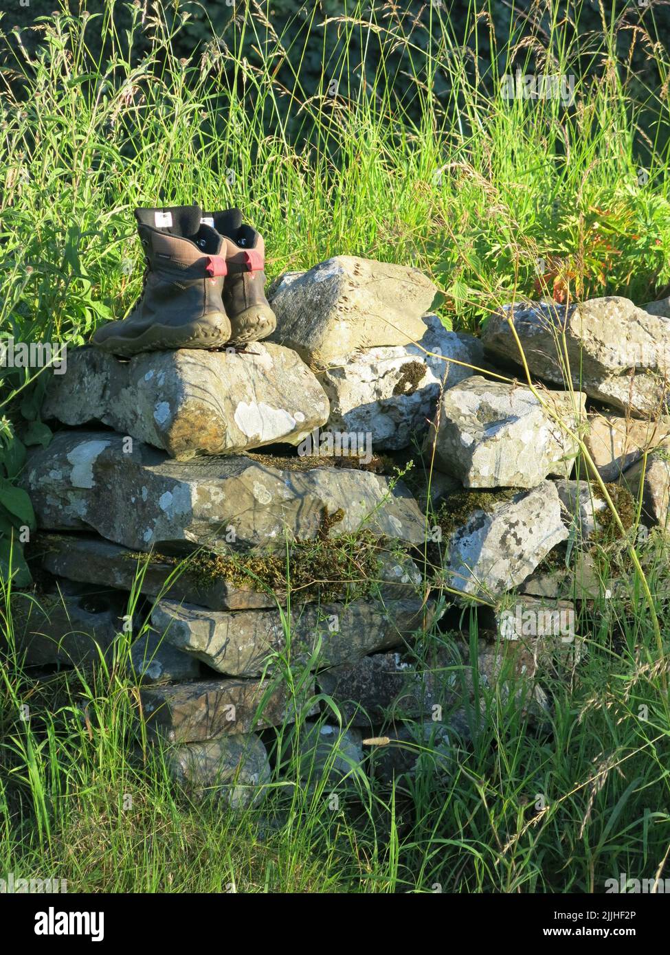 Wandern im Lake District: Foto eines Wanderstiefelspaares, das auf einer Steinmauer in der englischen Landschaft in der Nähe von Crooklands in Cumbria zurückgelassen wurde. Stockfoto