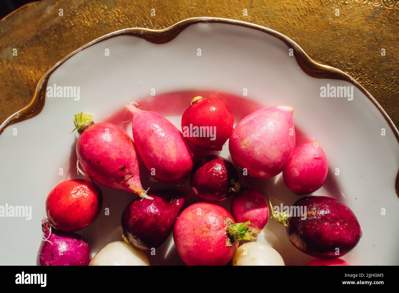 Getrimmt rosa, rot, lila, weiße Radieschen auf weißem Teller mit Gold Stockfoto
