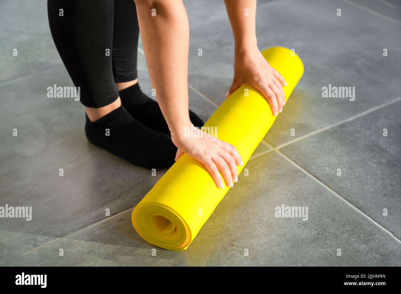 Mädchen bereitet sich darauf vor, die gelbe Rolle der Sportmatte für die Fitness auszupacken. Die Hände liegen aus nächster Nähe auf der Matte. Konzept eines gesunden Lebensstils. Stockfoto