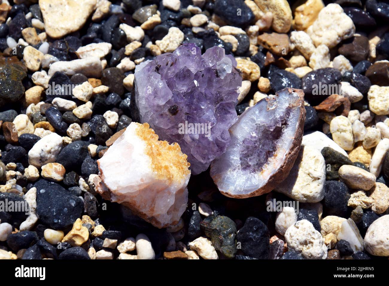 Eine schöne Druse und Geode aus Amethyst und Druse aus Citrin liegen auf nassen Steinen am Meer. Kristalle von Halbedelsteinen in der Sonne. Stockfoto