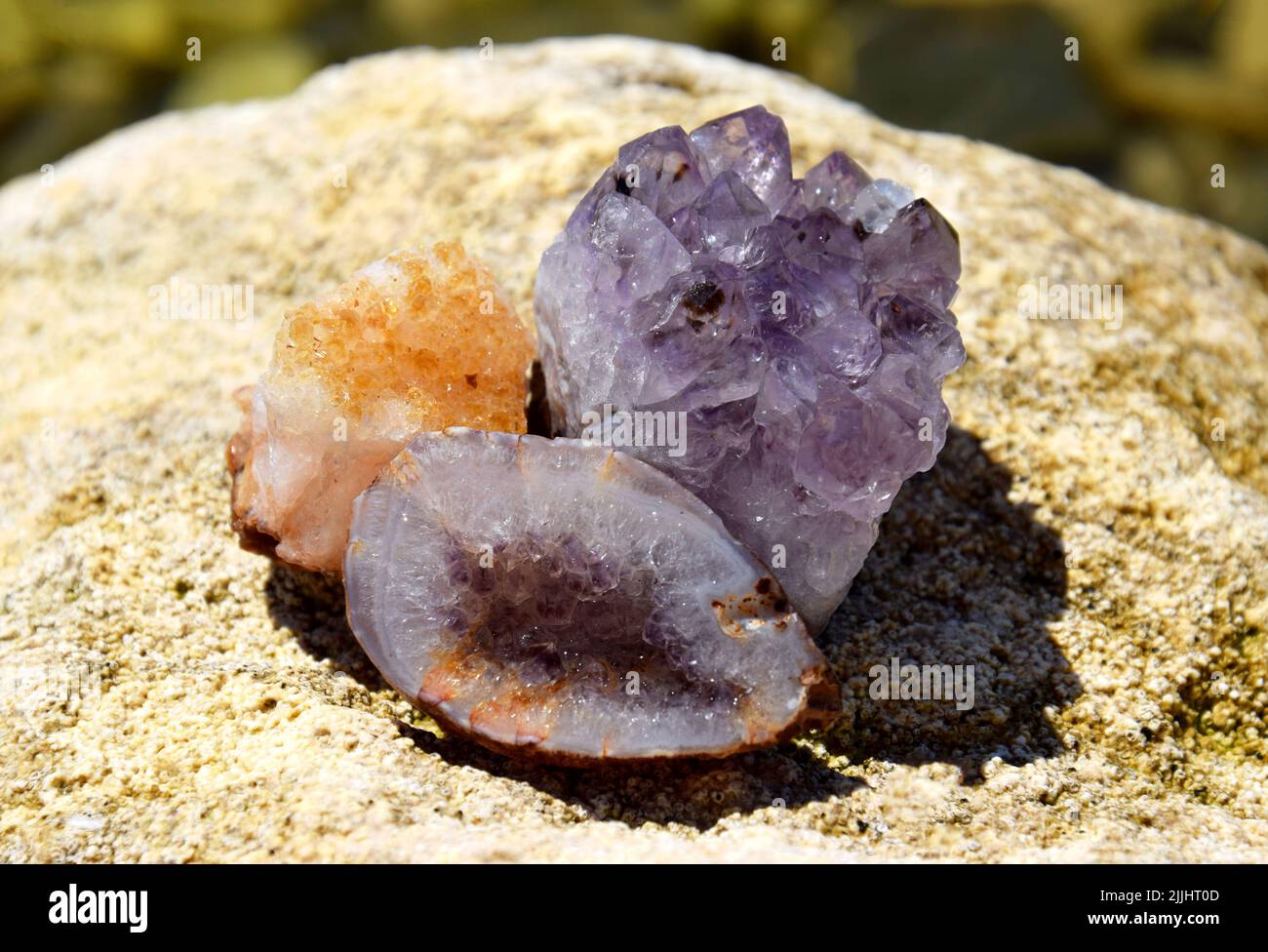 Eine schöne Druse und Geode aus Amethyst und Druse aus Citrin liegen auf einem Stein. Kristalle von Halbedelsteinen in der Sonne. Stockfoto