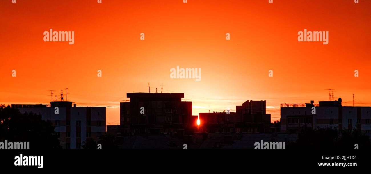 Silhouette der Stadt bei Sonnenuntergang. Die Sonne geht über hohen Gebäuden auf. Dramatischer Himmel in Sonnenstrahlen. Stadtlandschaft bei Sonnenaufgang. Kopierbereich, Bannerformat. Stockfoto