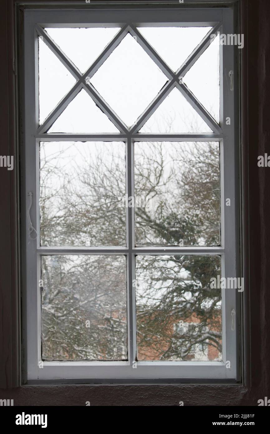 Nahaufnahme eines Glasfensters von innen, mit Blick auf das kalte Wetter am Morgen. Eine Holzfensterscheibe mit schlechter Isolierung, geschlossen und mit einem geschlossen Stockfoto