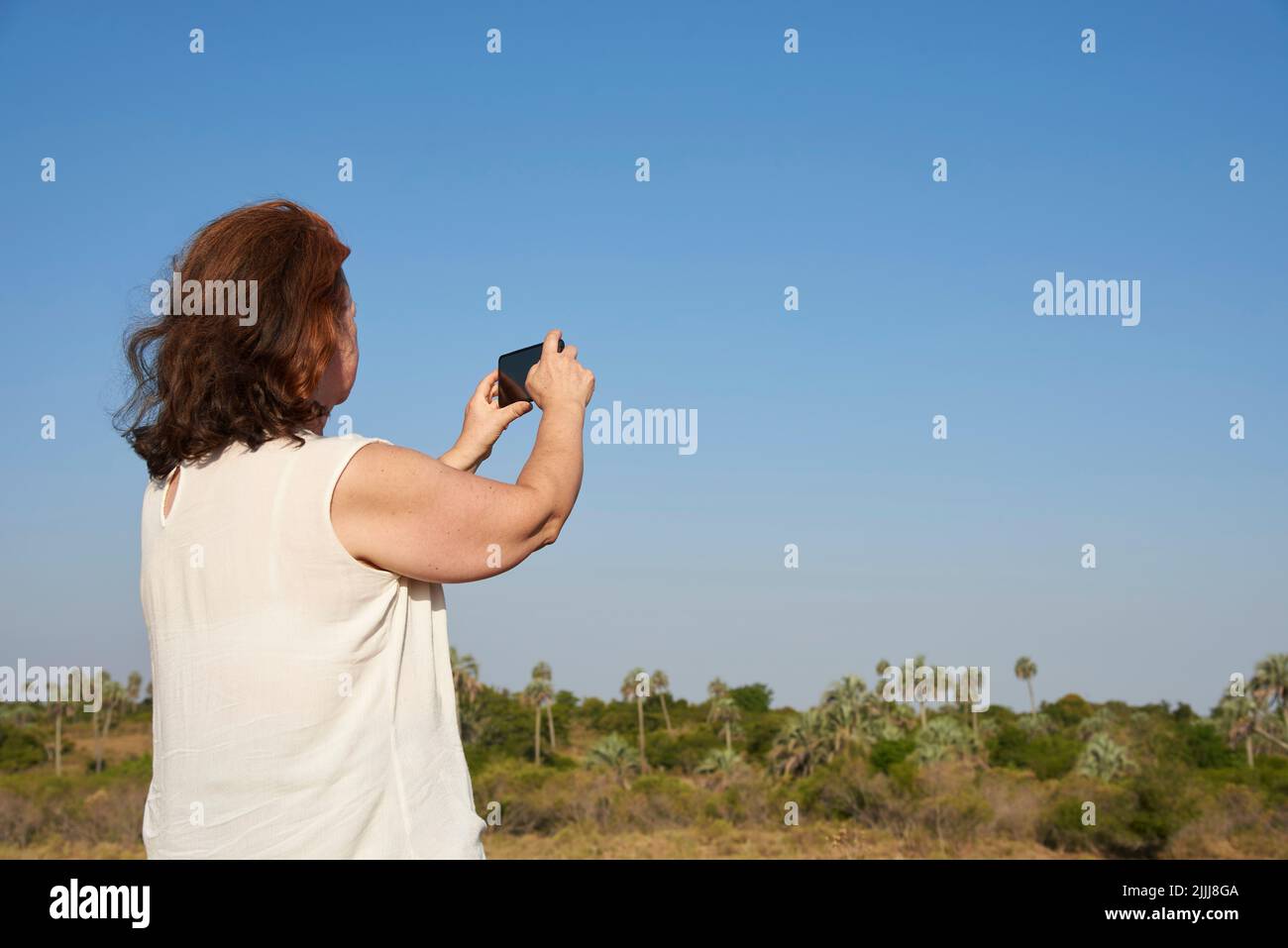 Rückansicht einer reifen Frau, die mit ihrem Telefon Fotos im El Palmar Nationalpark, Entre Rios, Argentinien, macht. Konzepte: Naturreisen, Urlaubsbilder Stockfoto