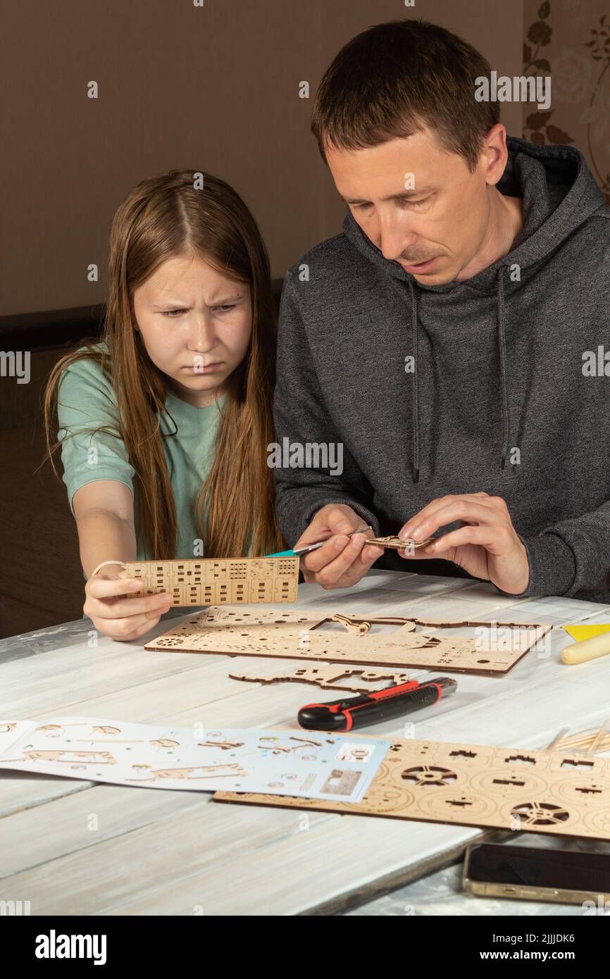 Erwachsener Mann, der Tochter im Teenageralter beibringt, mit Holz zu arbeiten. Ernsthaftes Kind und Vater schauen sich Anweisungen und hölzerne Details an. Konzentrierter Vater und Tochter Stockfoto