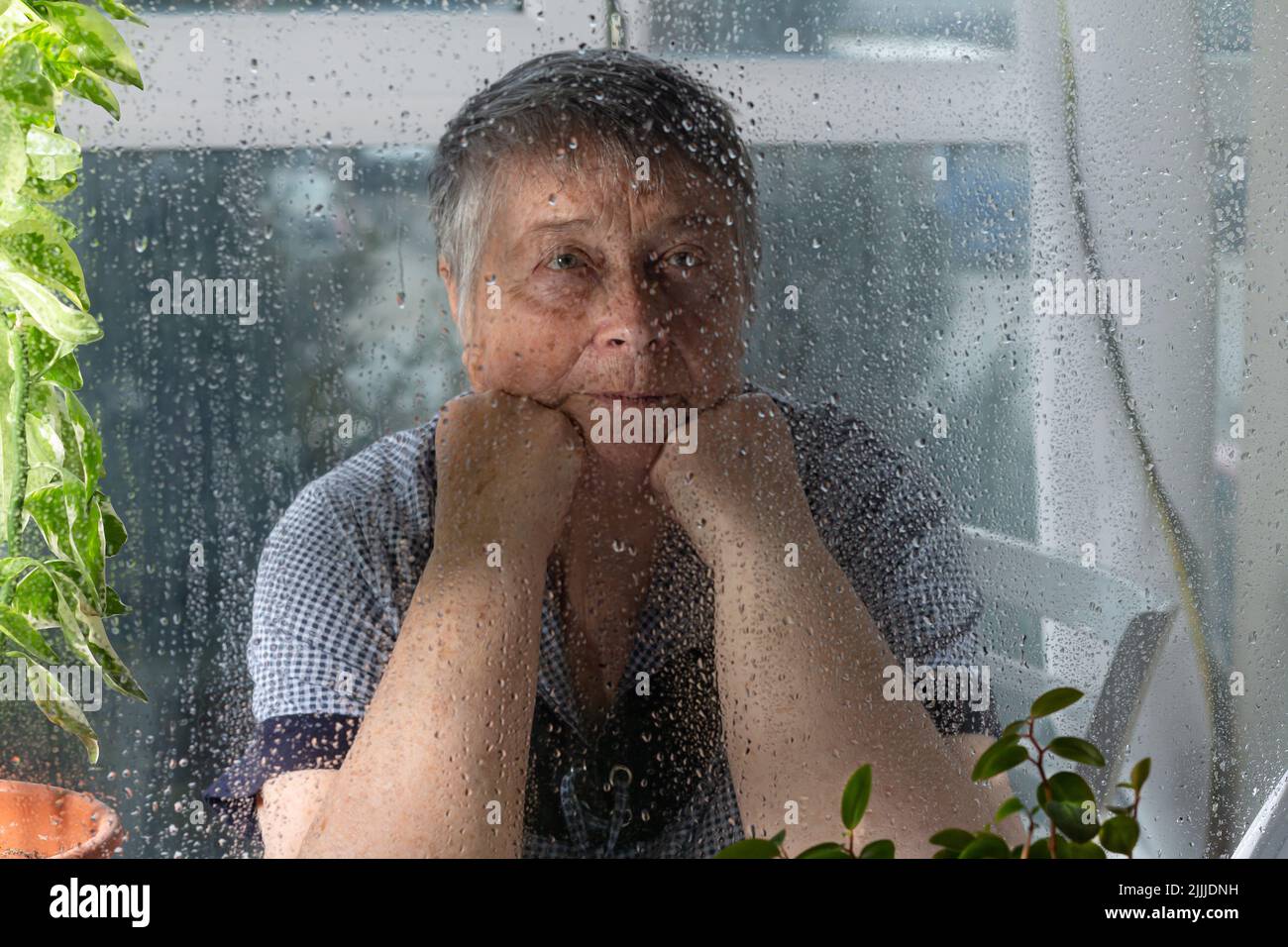 Weibchen in tiefem Denken schaut durch das Glas. Selektiver Fokus. Einsame Frau wartet auf ihre Kinder am Tag der Eltern. Globaler Tag der Eltern Stockfoto