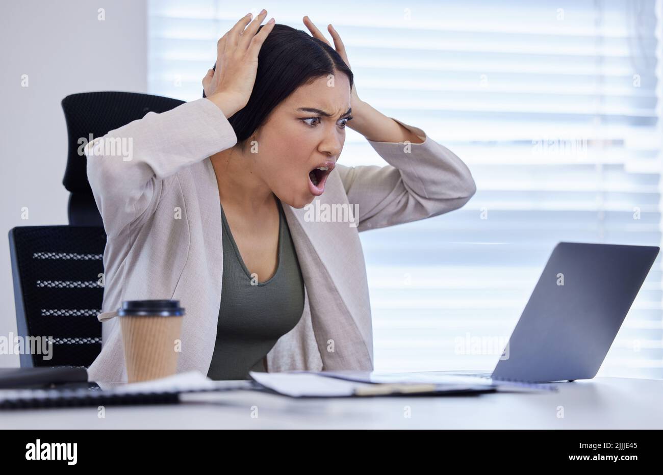 Gerade als Sie dachten, dass es sicher sei, sich abzumelden. Eine junge Geschäftsfrau, die wütend aussuht, während sie in einem modernen Büro einen Laptop benutzt. Stockfoto