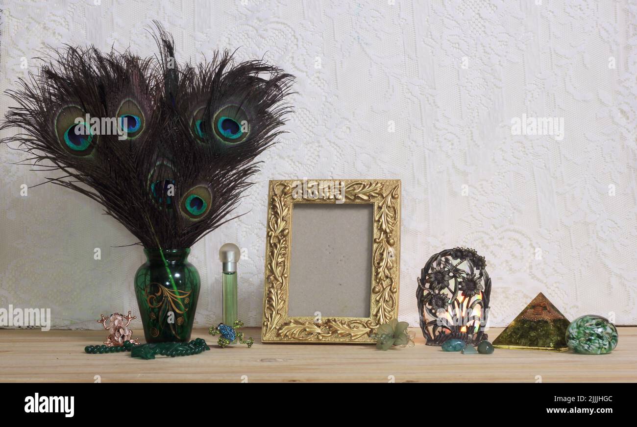 Vase aus Pfauenfedern mit grünem Schmuck und goldenem Bilderrahmen auf dem Tisch mit Spitzenhintergrund Stockfoto
