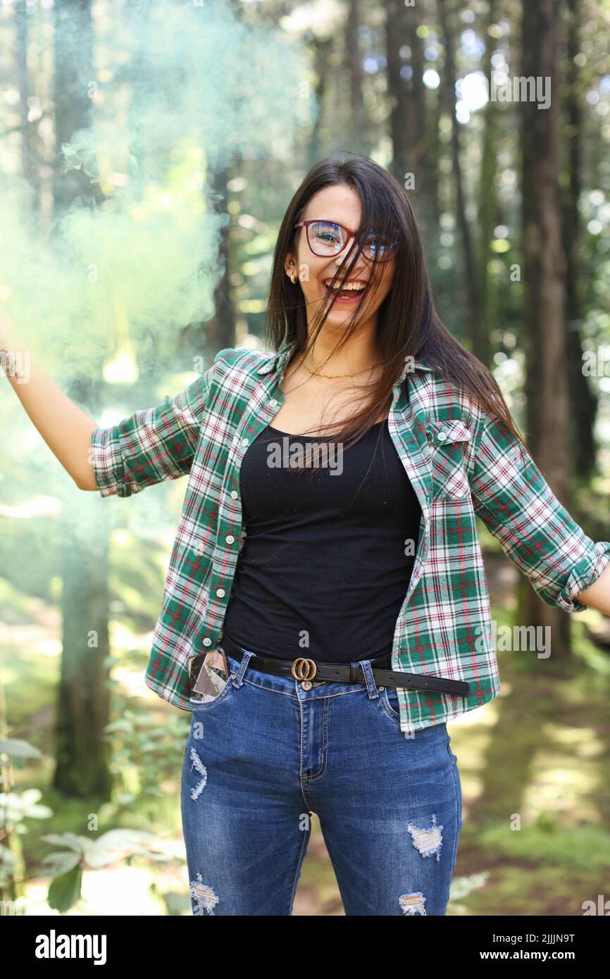 Junge Frau in einem Fotoshooting hob ihre Hand mit einer gelben Rauchbombe im Wald und lächelte Costa Rica an Stockfoto