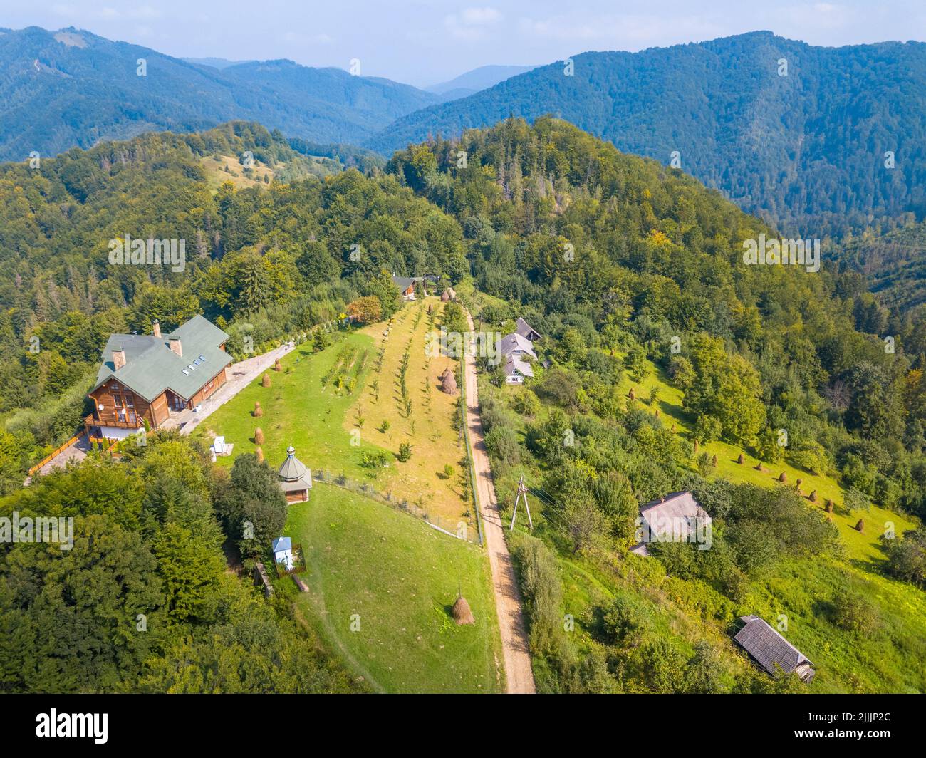 Sonniger Sommertag in den ukrainischen Karpaten. Ein modernes Bauernhaus auf einem Hügel, umgeben von Bergen. Luftaufnahme Stockfoto