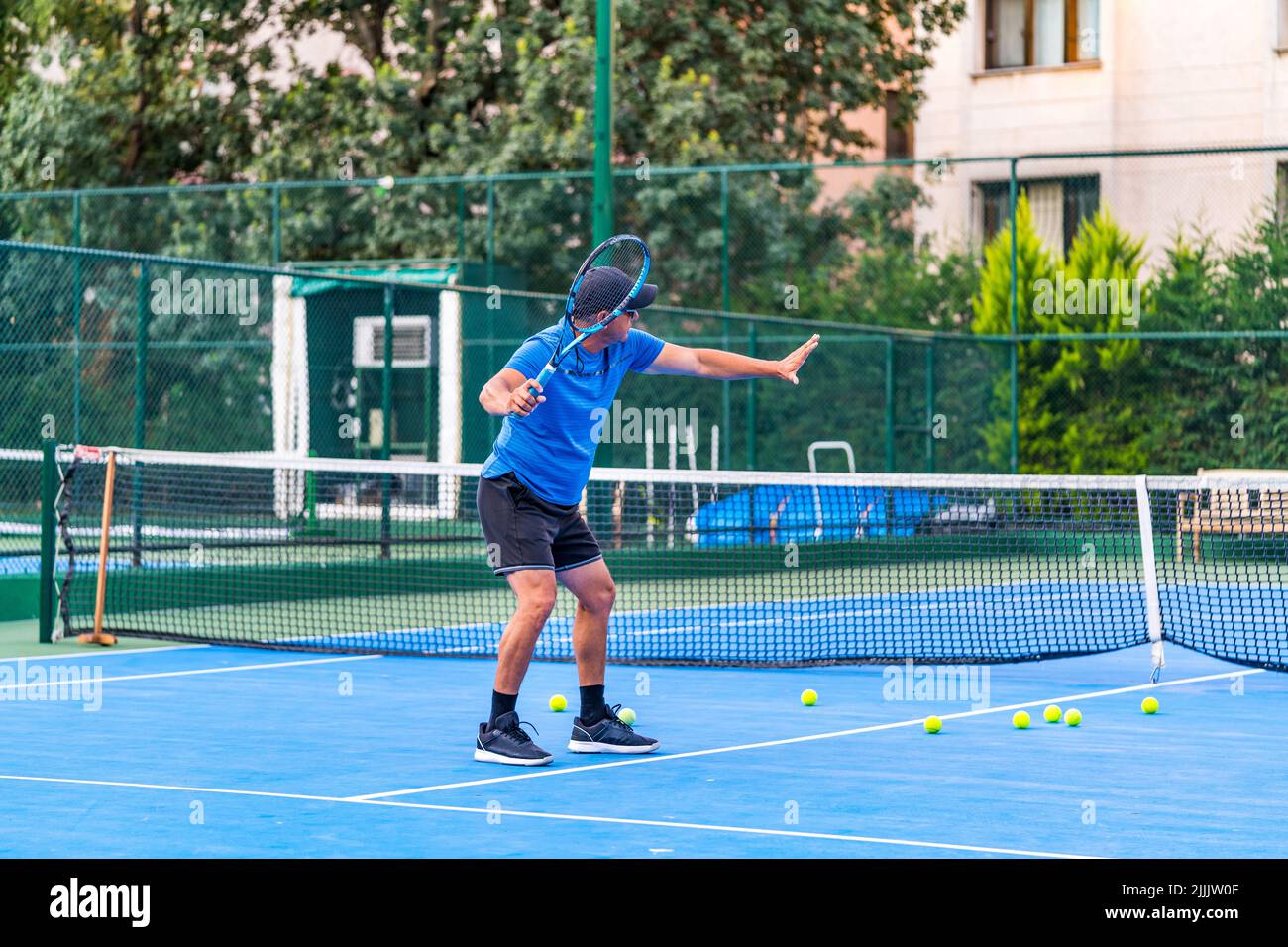 Mittlerer Alter positiver männlicher Tennisspieler Trainer mit Schlägertraining auf Hartplatz. Sonnenbrille Stockfoto
