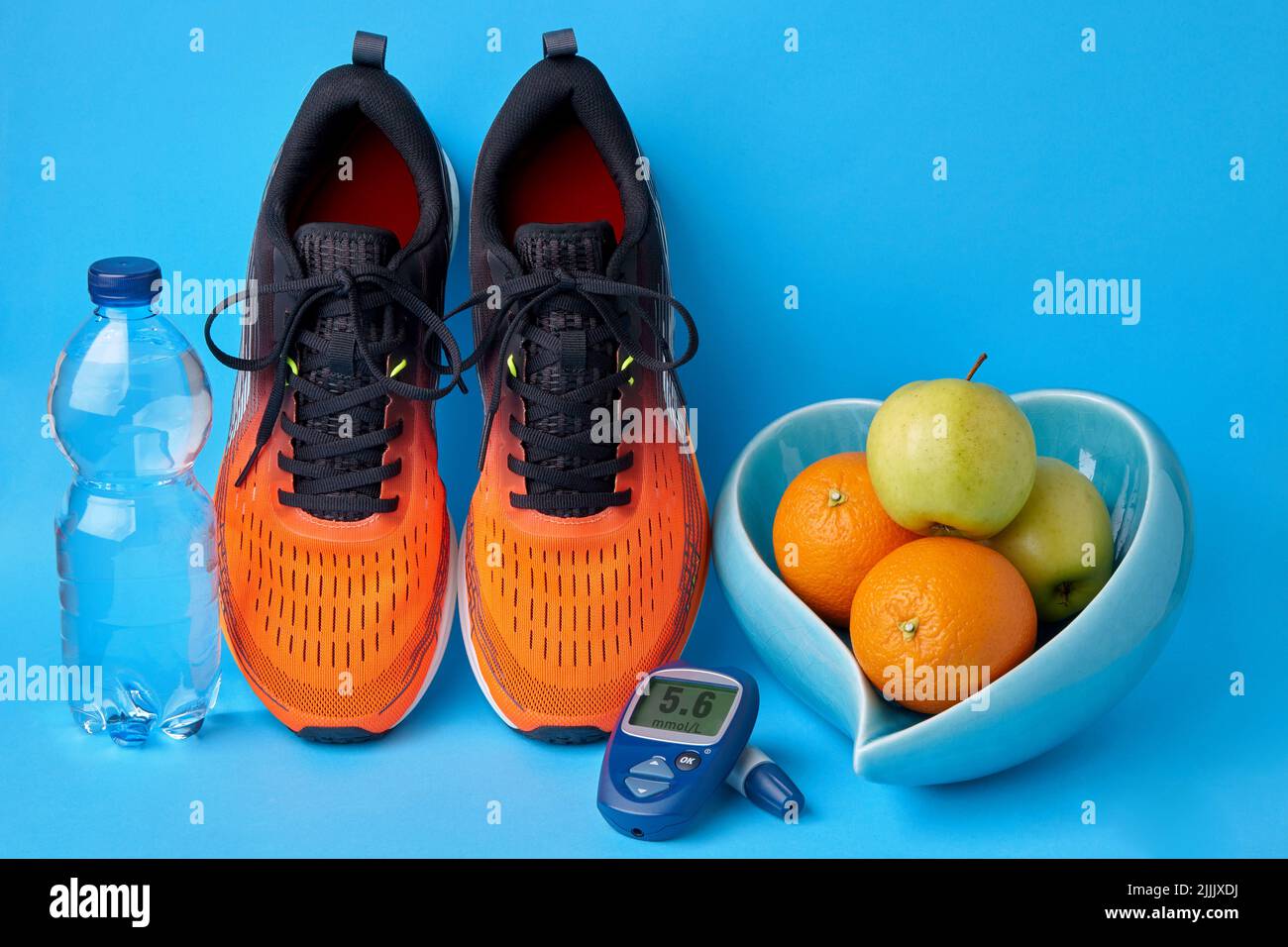 Orangefarbene Turnschuhe, Glucometer, Flasche Trinkwasser und Früchte auf blauem Hintergrund Stockfoto