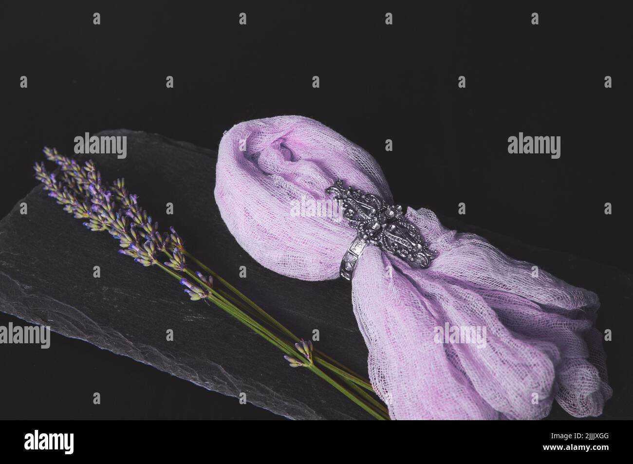 Lavendelstrauß auf einem schwarzen Brett aus rohem Stein mit einer Serviette auf dunklem Grund Stockfoto