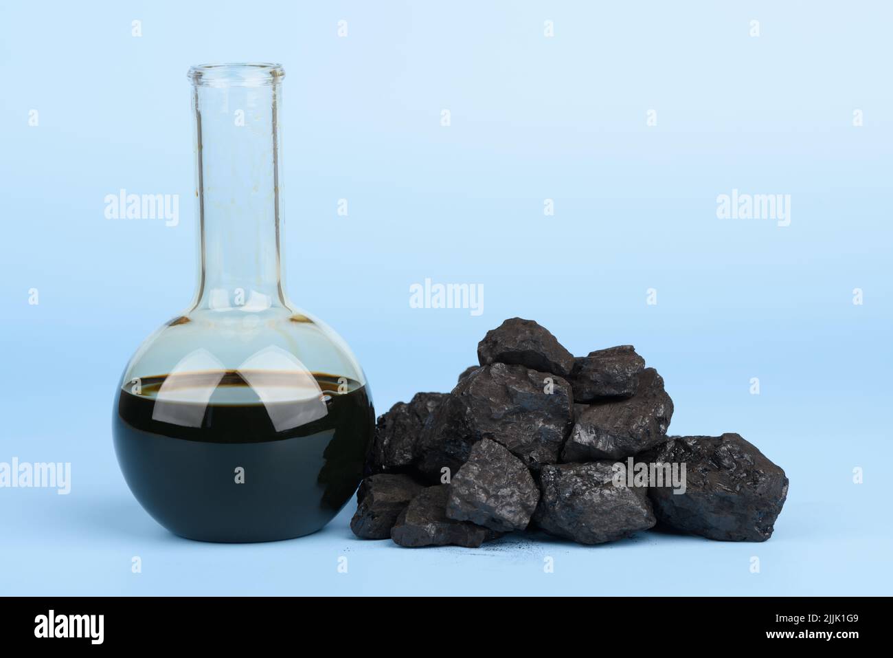 Rohöl im Glasbecher und schwarze Steinkohleklumpen auf blauem Hintergrund, Konzept fossiler Brennstoffe Stockfoto