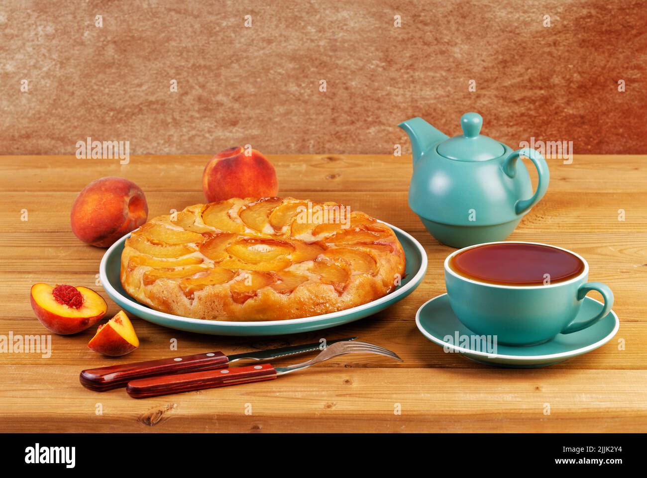 Hausgemachter Kuchen mit Pfirsichen und einer Tasse Tee auf einem Holztisch. Copyspace. Stockfoto