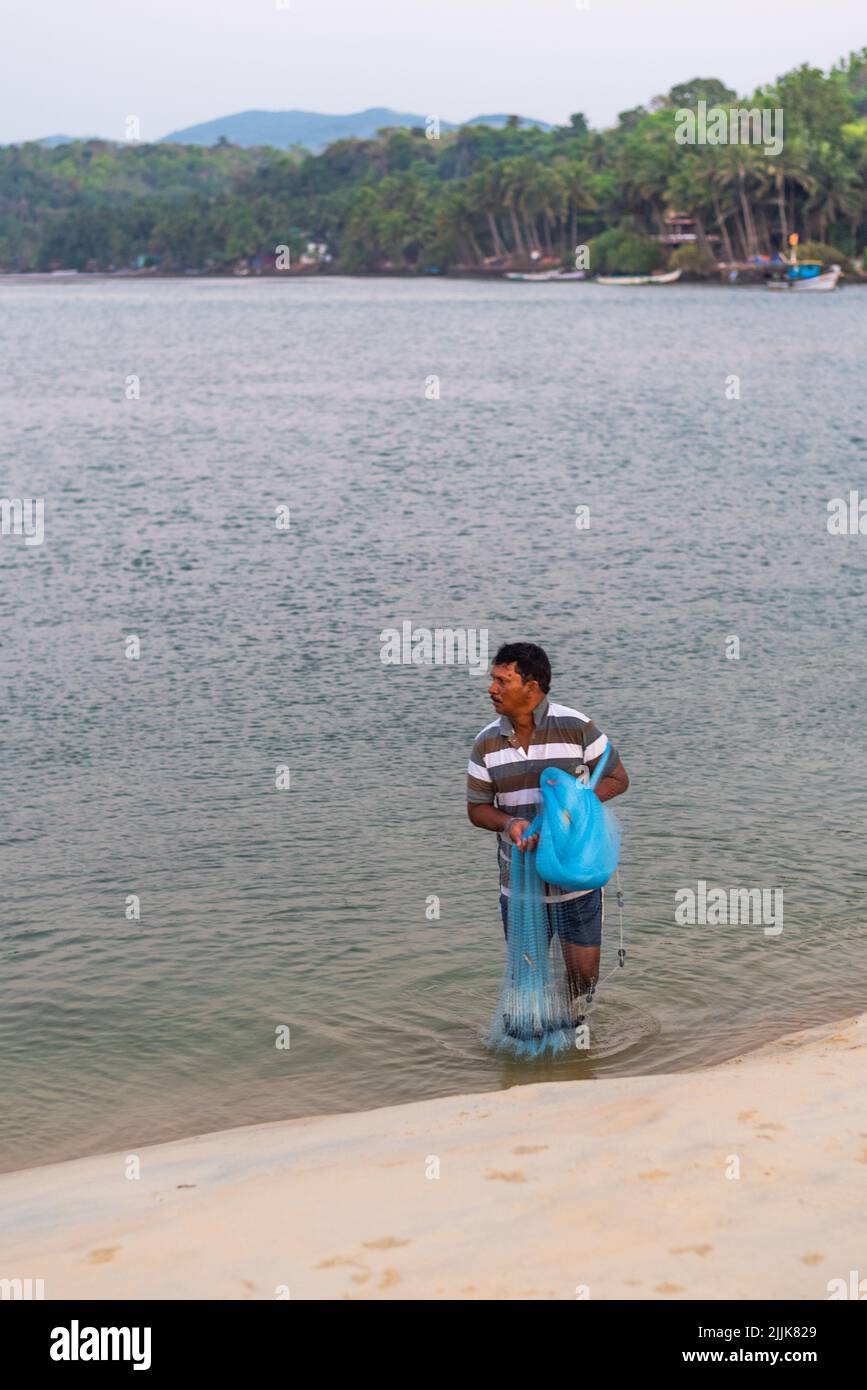 Eine vertikale Aufnahme eines lokalen indischen Fischers, der in Betul, Salcete, Goa, Indien, ein Netz in den Ozean wirft Stockfoto
