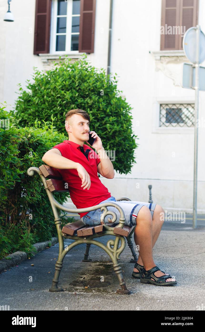 Junger, gutaussehender Mann, Tourist, der im Sommerpark spazierengeht, Altstadt. Telefonanruf. Technologie. Soziale Medien. Urlaub. Online arbeiten Stockfoto