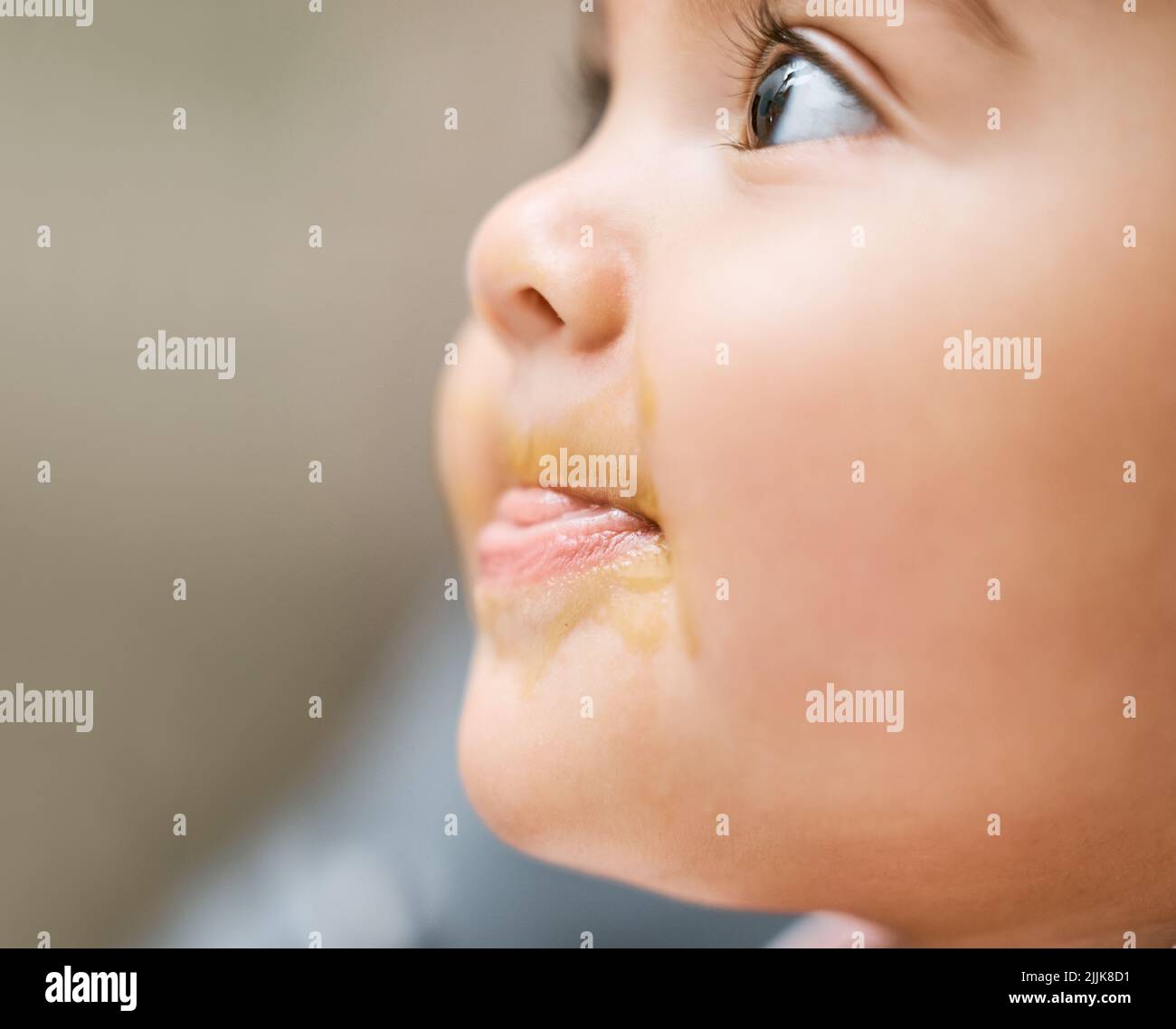 Es ist mein erstes Mal, etwas so leckeres zu versuchen. Ein entzückendes Baby Mädchen Mund mit Babynahrung bedeckt. Stockfoto